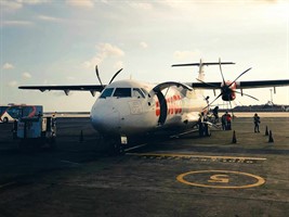 A plane on a runway, being loaded with cargo at sunset as people stand nearby.